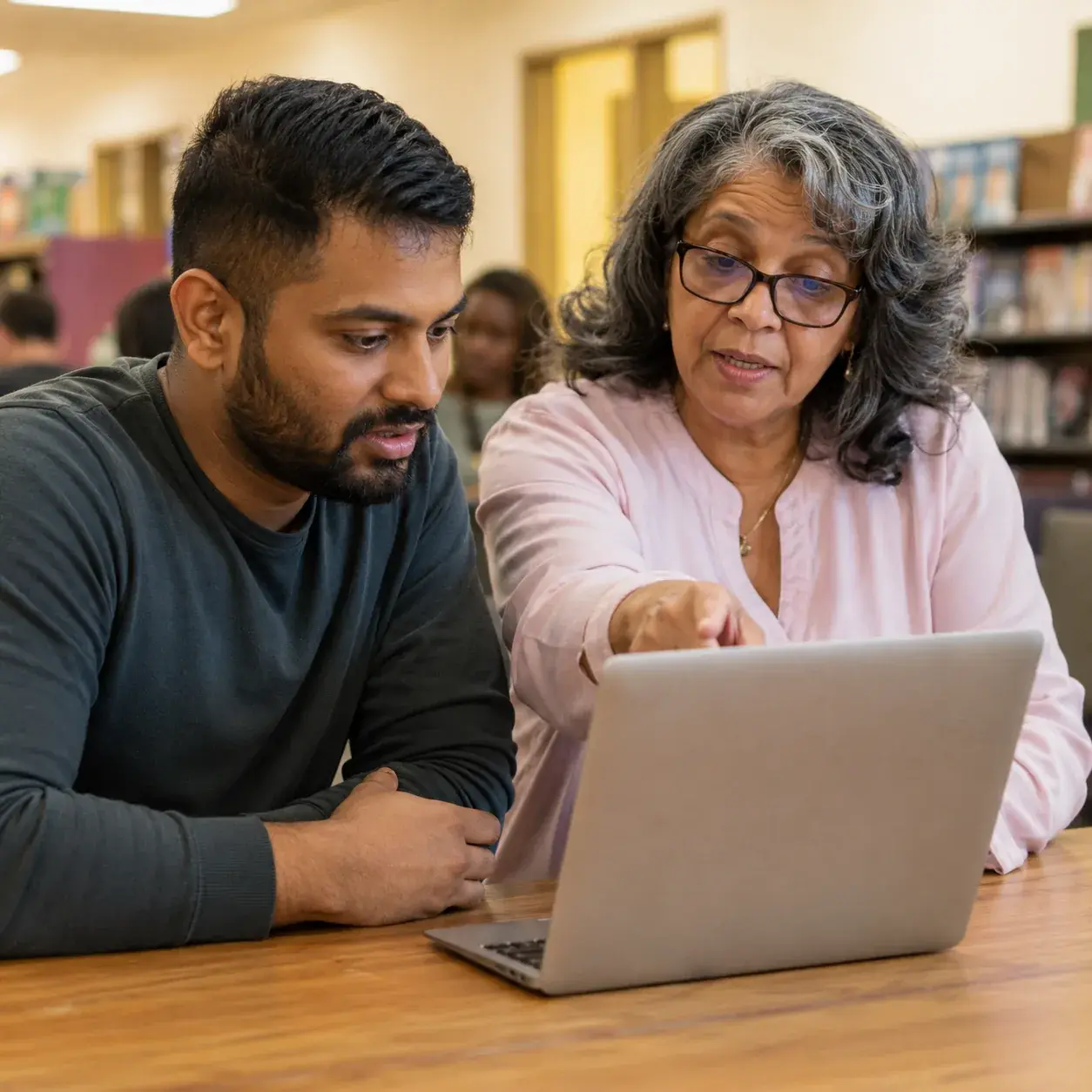 A mentor pointing at a laptop screen while working one-on-one with a participant in a library